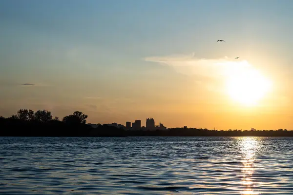 Şehrin arka planına karşı nehir kıyısında gün batımı.
