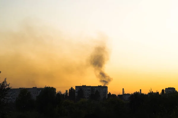 Günbatımı arka planında çok katlı bir bina. Siyah dumanlarla kaplanmış ateşten yükselen.