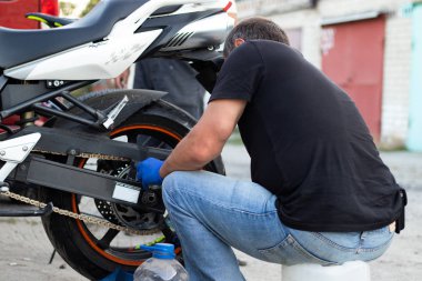 Motosiklet parçaları ve zincirleriyle ilgilenen bir adam. Yan görünüm.