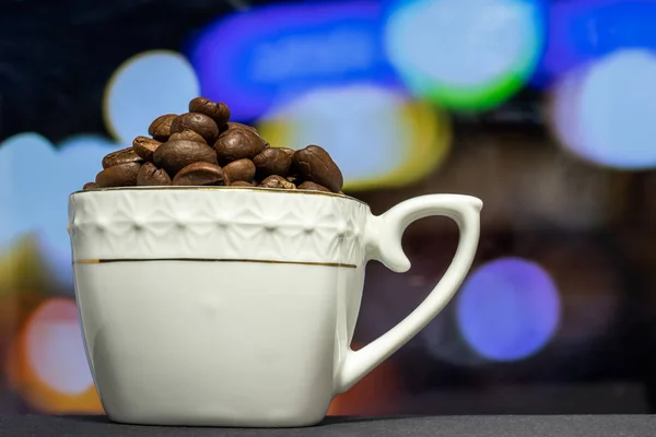 Kahve çekirdekleri ile doldurulmuş beyaz porselen bardak. Bulanık renk arkaplanı olan yakın plan..