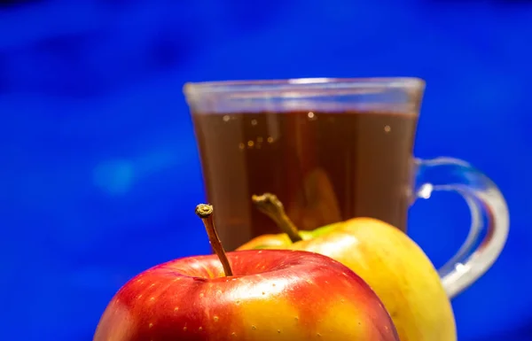 Two apples and a glass of juice. Close-up on a colored background.