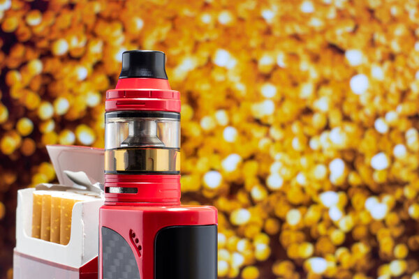 Вэйп и открытая пачка сигарет. Крупный план с цветным фоном
.