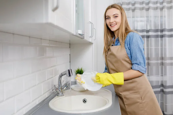 Симпатичная девушка моет посуду в светлом китчене — стоковое фото