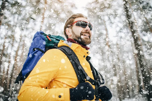 Gelukkige mannelijke wandelaar gaat door sneeuwval in het bos — Stockfoto