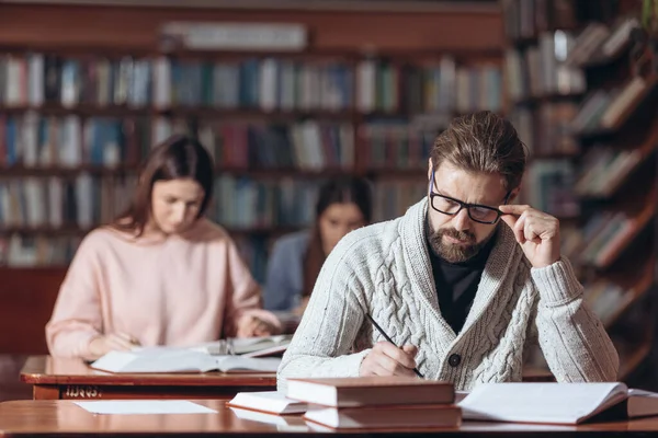 Gammal skäggig man som sitter på biblioteket med böcker — Stockfoto