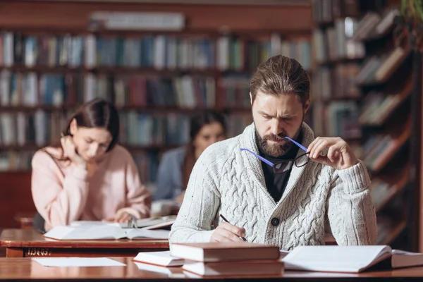 Konzentrierter Mann macht sich Notizen beim Bücherlesen in der Bibliothek — Stockfoto