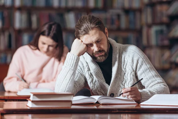 Trött skäggig man sover på biblioteket — Stockfoto