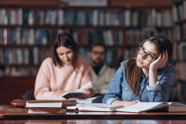 Söt flicka drömmer om fest medan du studerar på biblioteket — Stockfoto