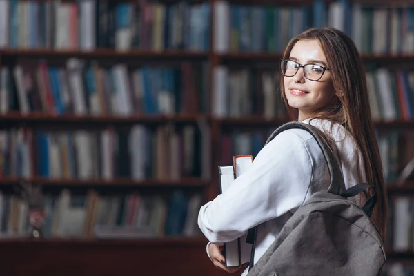 Glada student stående i universitetsbiblioteket med böcker — Stockfoto