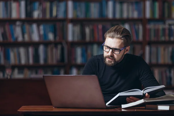 Starší neoholený muž pomocí notebooku, zatímco sedí v knihovně — Stock fotografie