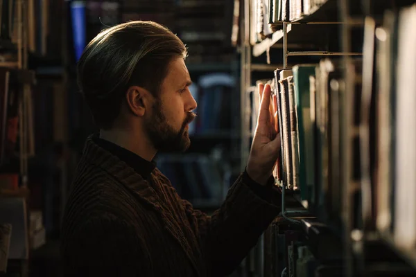 Boční pohled na vousatého muže při výběru knihy ve veřejné knihovně — Stock fotografie