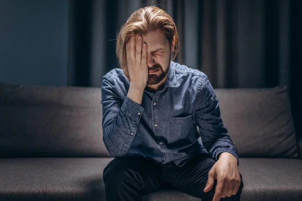 Middle-aged man crying alone at living room without lights