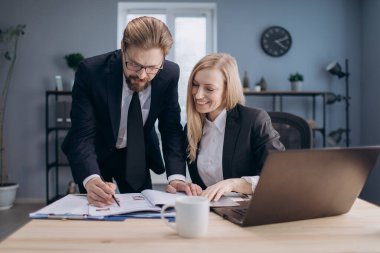 Olgun patron sekreterin yanında duruyor ve belgeleri imzalıyor.
