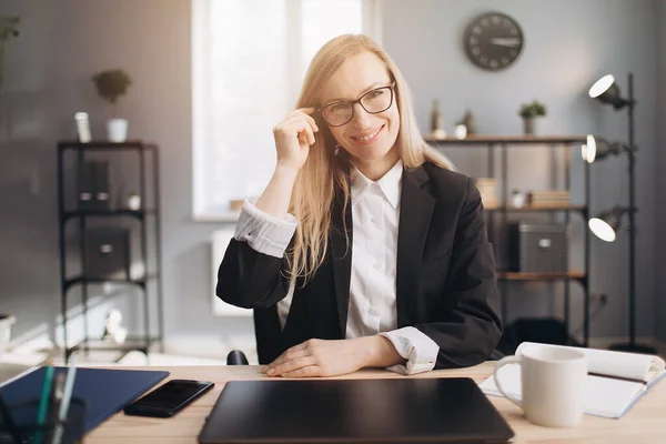 Modern ofiste oturan, gözlüklü, gülümseyen kadın. — Stok fotoğraf
