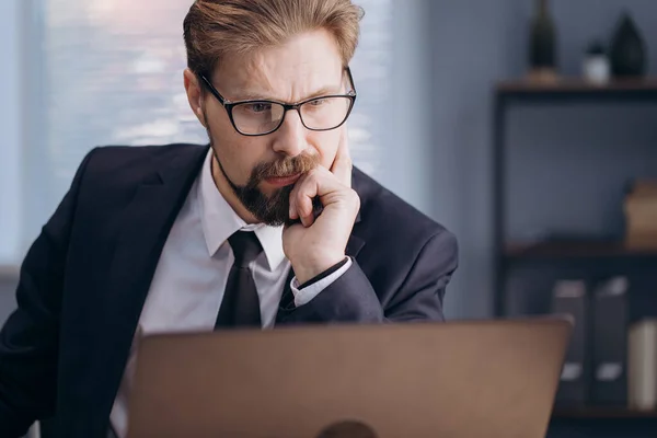 Pozorný vousatý muž pracující na notebooku v kanceláři — Stock fotografie