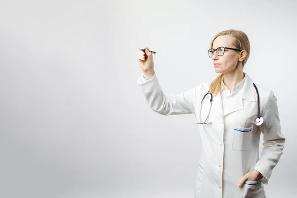 ผู้หญิงในชุดแพทย์ชี้ด้วยปากกาบนพื้นที่ว่างเปล่า — ภาพถ่ายสต็อก