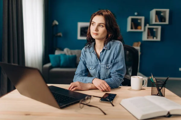 Genç kız dizüstü bilgisayarla masada oturuyor ve gözlerini kaçırıyor. — Stok fotoğraf