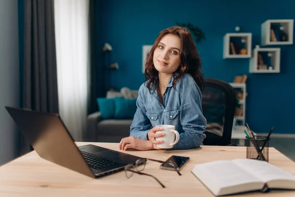 Flicka tittar på kameran när du sitter vid bordet med laptop — Stockfoto