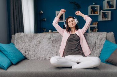 Genç bir kadın kanepede oturup müzik dinliyor.