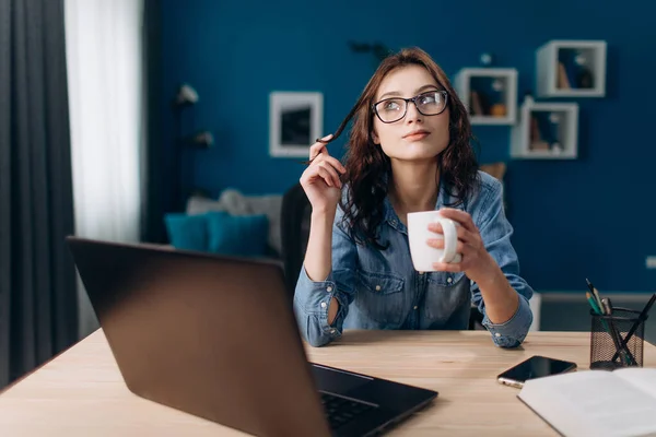 Güzel bir kadın evde dizüstü bilgisayarla oturup kahve içiyor. — Stok fotoğraf