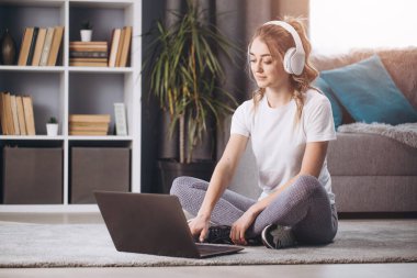 Atletik kız dizüstü bilgisayarı ve kulaklıklarıyla yerde oturuyor.