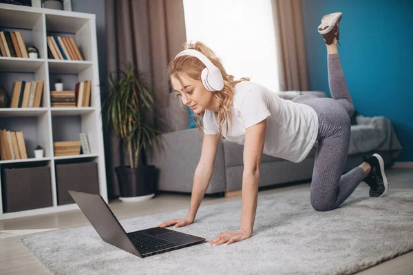 Mujer deportiva en auriculares piernas de entrenamiento en casa —  Fotos de Stock