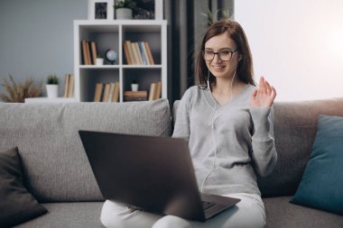 Bilgisayarda internette konuşurken kanepede oturan kız.