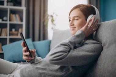 Kız kanepede dinleniyor ve kulaklıkla müzik dinliyor.