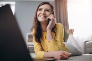 Neşeli kız yerde yatarken telefonla konuşuyor.