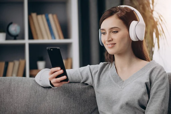 Mujer sentada en un sofá con auriculares y escuchando música — Foto de Stock