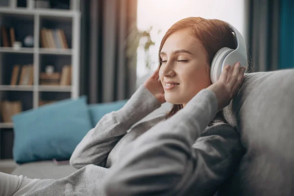 Jovencita relajada sentada en un sofá con auriculares — Foto de Stock