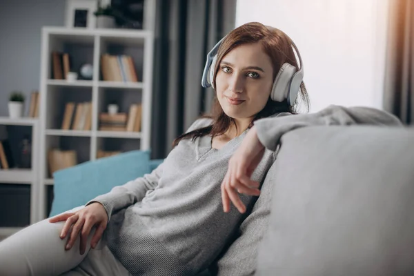 Mujer atractiva en auriculares mientras está sentado en un sofá acogedor — Foto de Stock
