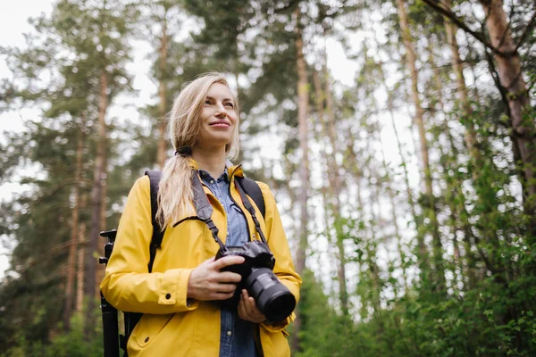 Vrolijke vrouw staat bij het voorjaar bos met digitale camera — Stockfoto