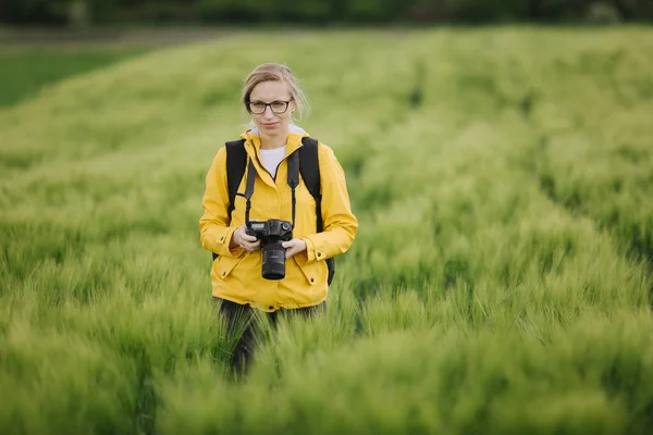 Blond fotograaf wandelen tussen tarweveld met camera — Stockfoto