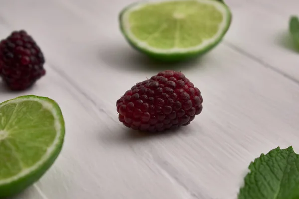 Böğürtlen ve limon dilimleri ve beyaz ahşap üzerinde nane.