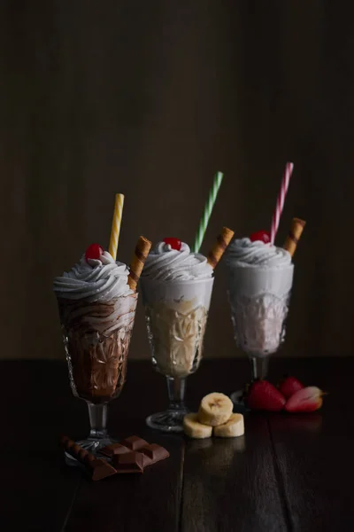 Kahverengi ahşap masada kirazlı ve kremalı meyveli ve çikolatalı milkshake.