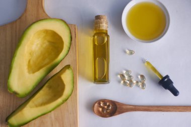 Beyaz arka plan ve e vitamini kapsüllü cam şişede avokado yağı.