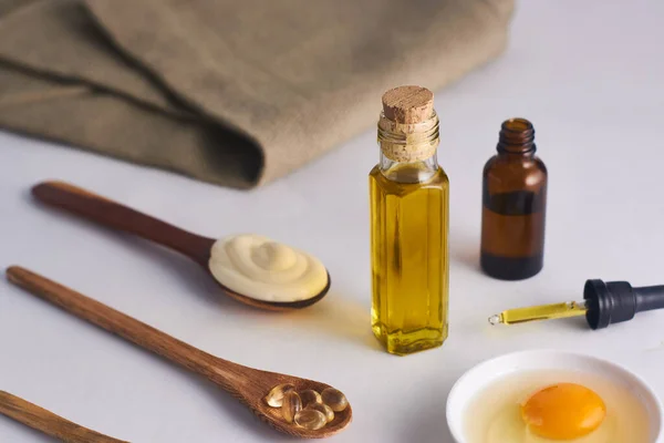 Cam kavanozda zeytinyağı maskesi ve kaşıkta mayonez ve beyaz arka planda E vitamini.