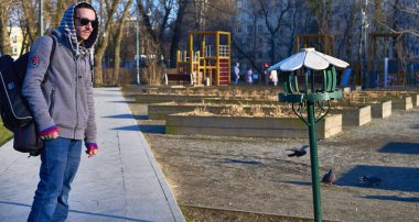 Kuş yemliğinin yanında sırt çantalı bir adam var.