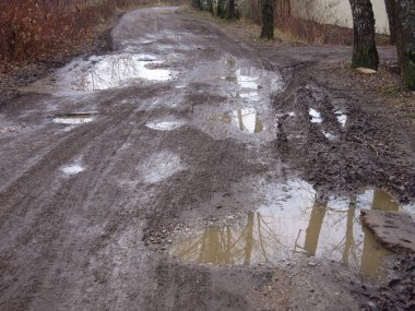 Rus köyünde sonbaharda su birikintileri, çukurlar ve kille dolu bozuk bir yol.