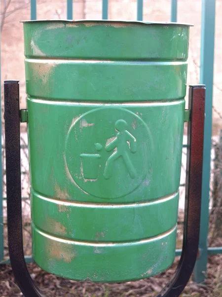 green metal street urn with the sign of a person throwing garbage
