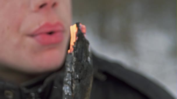 Un joven sosteniendo ramitas ardiendo y avivando el fuego. Movimiento lento . — Vídeo de stock
