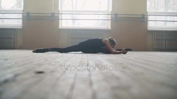 Beautiful graceful ballerine in black practice split ballet position in class room background. — Stock Video