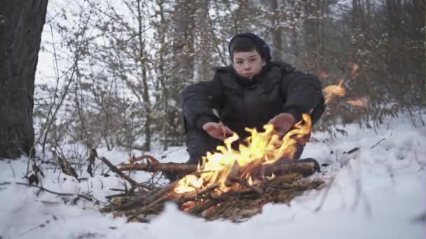 Маленький мальчик в нищете, согретый огнем в холодном зимнем лесу — стоковое видео
