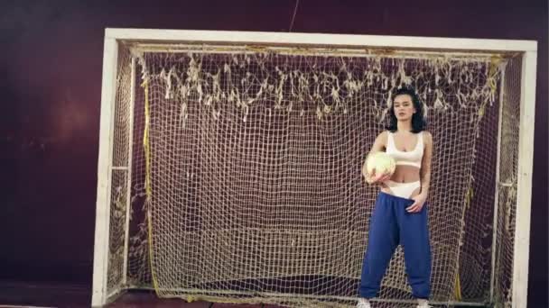 Όμορφο κορίτσι στέκεται με μια μπάλα ποδοσφαίρου στην πύλη του στο γυμναστήριο του σχολείου — Αρχείο Βίντεο