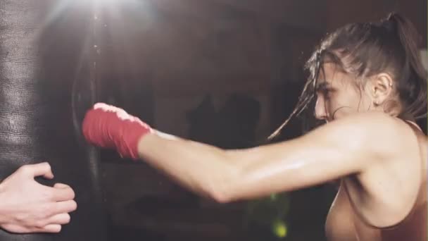Hermosa mujer perforando una bolsa de boxeo con guantes de boxeo en el gimnasio. Concepto sobre deporte, fitness, artes marciales y personas — Vídeos de Stock