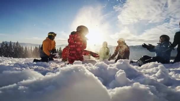 Happy groupof skiers having fun sitting in snowdrift with snowboards and tossing snow — Stock Video