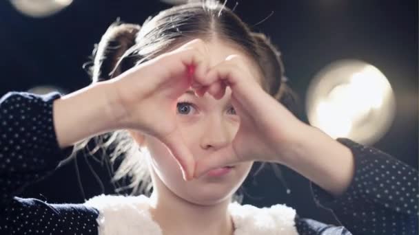 Ευτυχισμένος κορίτσι διπλωμένα τα χέρια της μια καρδιά σχήμα και φαίνεται στην κάμερα μέσω του. — Αρχείο Βίντεο