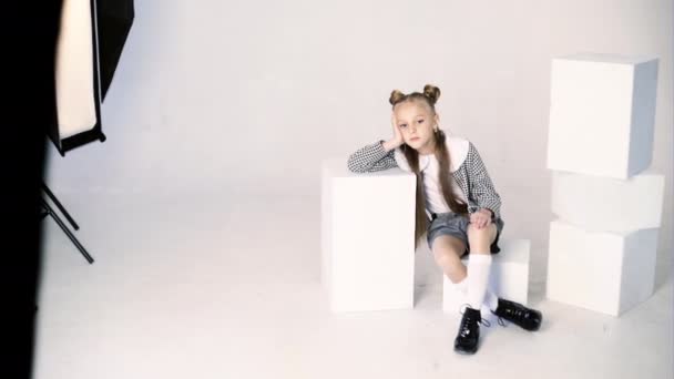 Menina joga em uma cadeira branca no estúdio em uma sessão de fotos . — Vídeo de Stock
