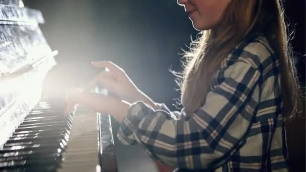 Vacker flicka som leker på piano i ett mörkt rum med en ljuskälla — Stockvideo